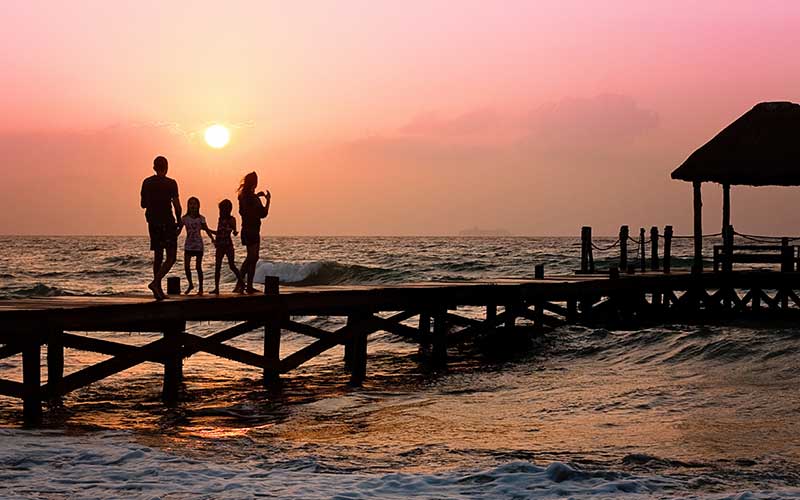 A family stands together on a pier, silhouetted against a vibrant sunset sky.