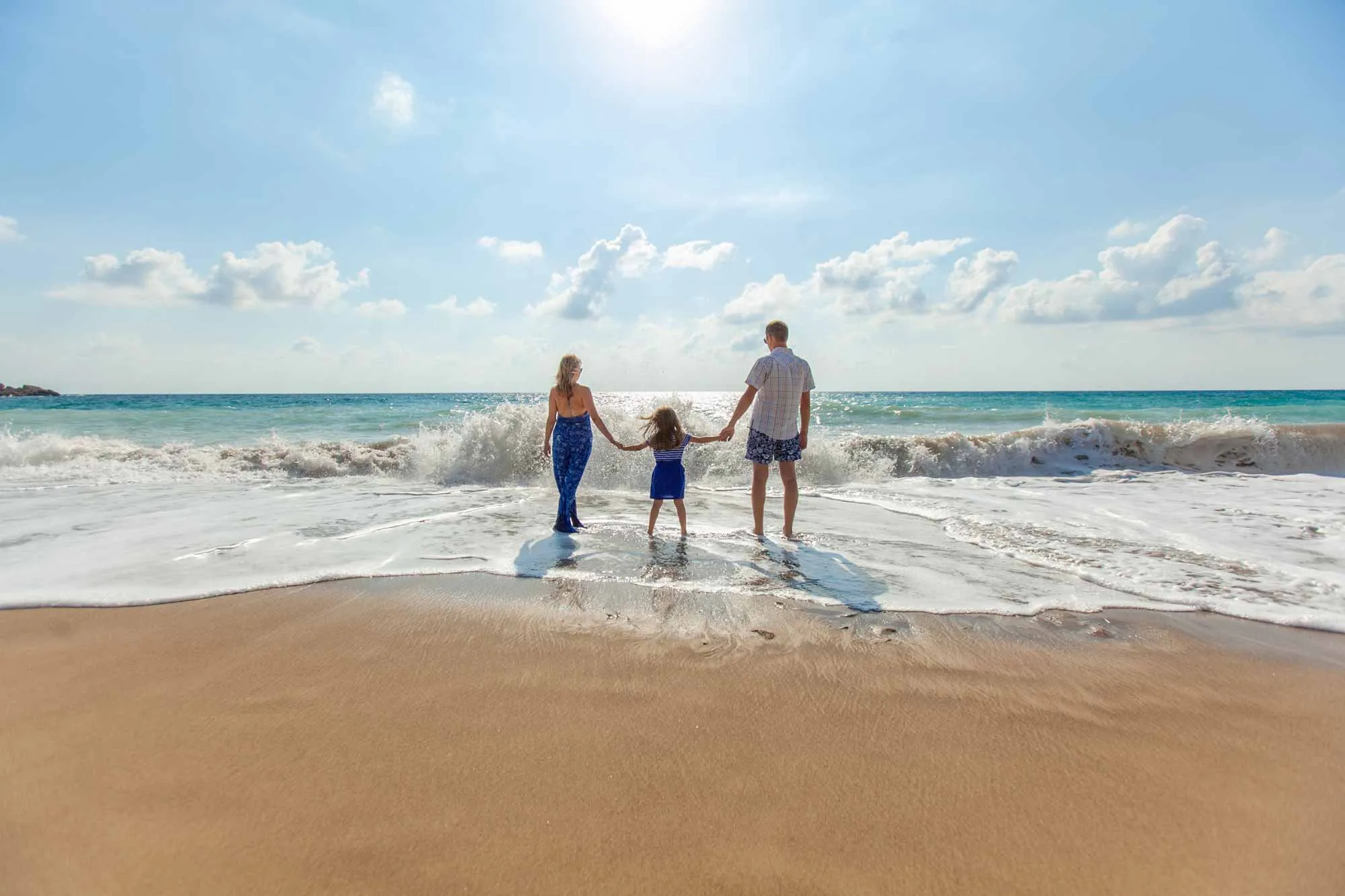 A family of four stands on the beach, holding hands and enjoying the ocean view together.